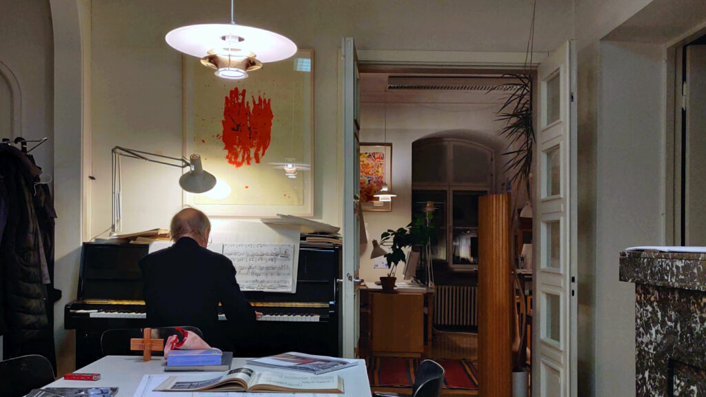 Mies soittaa arkkitehtitoimiston pianoa selin katsojaan.